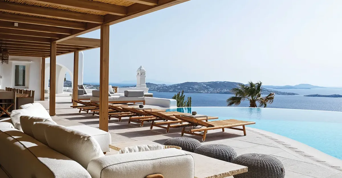 Luxury Mykonos villa terrace with wooden pergola overlooking the Aegean Sea, representing a €100K ultra-luxury summer experience with private villas, curated access, and high-end concierge services.